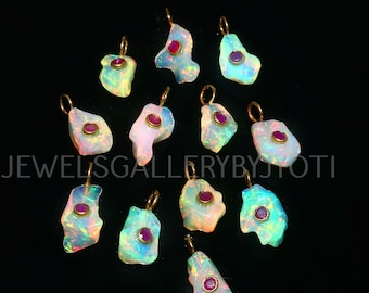 May include: A collection of opal pendants with gold-colored loops and small, round, red gemstones. The opals have a colorful, iridescent appearance, with shades of blue, green, and pink. The text "JEWELSGALLERYBYJYOTI" is visible.