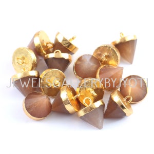 Puede incluir: Un grupo de 12 botones de piedra de sol marrón con engastes de metal dorado. Cada botón tiene una parte superior puntiaguda en forma de pirámide y un bucle para coser.
