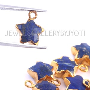 May include: A close-up of a set of gold-plated star-shaped charms with blue lapis lazuli stones. The charms have a loop at the top for attaching to jewelry.