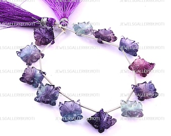 May include: Strand of carved fluorite flower beads in shades of purple, blue, and pink. The beads are strung on a silver wire and are connected to a purple tassel. The beads are approximately 1.25 inches in diameter.