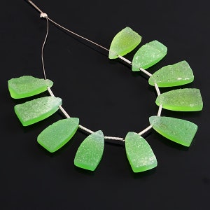 Puede incluir: Una hebra de cuentas de piedras preciosas verdes, cada cuenta tiene una forma irregular única con una superficie texturizada. Las cuentas están enhebradas en un alambre de plata.