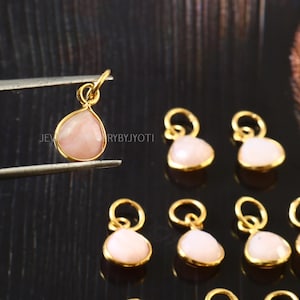 Puede incluir: Un grupo de 8 abalorios chapados en oro con piedras de ópalo rosa. Cada abalorio tiene forma de lágrima y tiene un bucle para sujetarlo a un collar o pulsera.