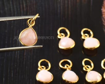 May include: A group of 8 gold-plated charms with pink opal stones. Each charm is shaped like a teardrop and has a loop for attaching to a necklace or bracelet.