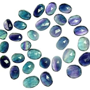 May include: A collection of 20 faceted oval-shaped fluorite gemstones in shades of blue, green, and purple. The stones are arranged in a spiral pattern on a white background.