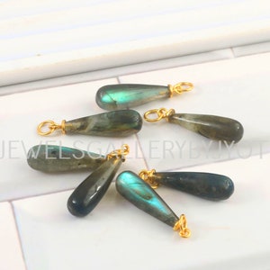 May include: Seven teardrop-shaped labradorite gemstone pendants with gold-toned jump rings. The gemstones are iridescent with shades of green and blue.
