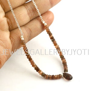 May include: A silver chain necklace with a brown gemstone pendant and brown gemstone beads. The necklace is approximately 18 inches long.