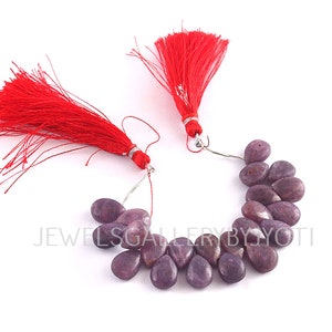 May include: A strand of purple gemstone beads in a teardrop shape. The beads are strung on a silver wire with red tassels on each end.