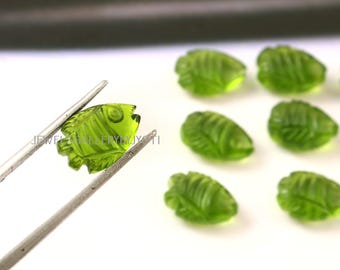 Puede incluir: Colección de cuentas de piedras preciosas verdes talladas. Una cuenta, sujeta con pinzas, muestra un diseño de pez. Otras cuentas presentan un diseño de hoja. Las cuentas translúcidas tienen tallas detalladas, para la creación de joyas.
