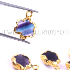 May include: Gold-plated flower charm with a purple, blue, and green fluorite gemstone. The charm has a loop at the top for attaching to jewelry.