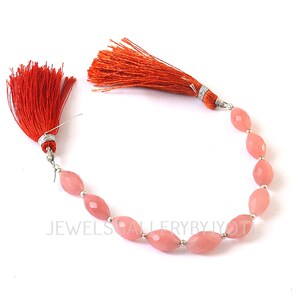May include: A strand of faceted, oval-shaped pink gemstones with silver-colored spacers. The gemstones are strung together with a bright orange tassel at each end. The tassels are made of fine threads and are attached with silver-colored metal.