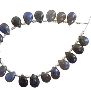 Könnte beinhalten: Eine Strähne aus tropfenförmigen Labradoritperlen, die auf silbernem Draht aufgefädelt sind. Die Perlen sind dunkelblau-grau mit irisierenden Schimmern.