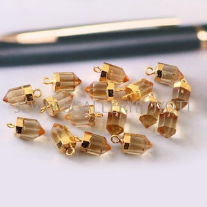 May include: A collection of 14 gold-plated crystal point pendants. Each pendant features a clear, faceted crystal with a gold-plated loop at the top. The crystals are approximately 2.5 cm in length.