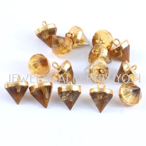 Könnte beinhalten: Eine Gruppe von 12 vergoldeten, facettierten, klaren Quarzkristall-Anhängern mit einer goldenen Öse oben. Die Anhänger haben die Form einer Pyramide.