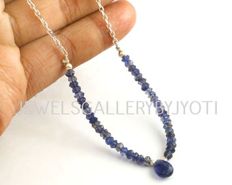 May include: A silver chain necklace with a blue gemstone pendant. The necklace is made of small, faceted blue gemstones and a larger, oval-shaped blue gemstone pendant.