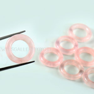 May include: A group of eight pink rose quartz rings, each with a smooth, polished finish. The rings are approximately 1 inch in diameter and are perfect for jewelry making or crafting.