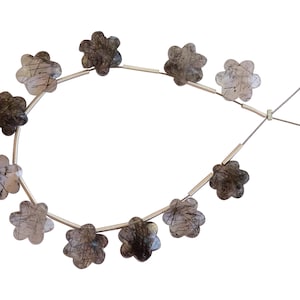 Puede incluir: Una hebra de cuentas de piedra de cuarzo negro y transparente en forma de flor. Las cuentas están enhebradas en un alambre plateado.