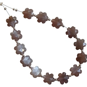 Puede incluir: Una hebra de cuentas de piedras preciosas de color marrón claro, cada cuenta tiene forma de flor con cinco puntas. Las cuentas están enhebradas en un alambre de plata.