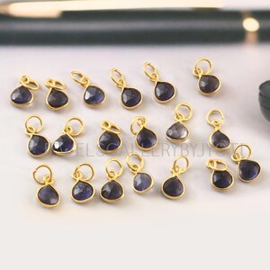 May include: A collection of 18 gold-plated charms featuring teardrop-shaped blue gemstones. Each charm has a loop for attaching to jewelry.