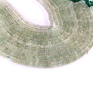 May include: A strand of light green faceted gemstone beads. The beads are small and round, and they are strung on a clear thread. The beads are arranged in a circular pattern, and they are all the same size.