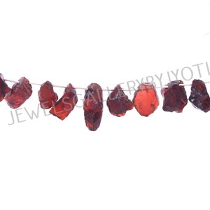 Puede incluir: Una hebra de cuentas de piedras preciosas rojas, probablemente granates, enhebradas en un alambre de plata. Las cuentas tienen una forma irregular y un aspecto natural y áspero. La imagen está etiquetada como "JEWELSGALLERYBYJYOTI".