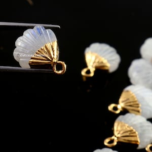 May include: A group of white moonstone shell charms with gold accents. The charms have a loop at the top for attaching to jewellery.