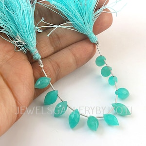 May include: Two strands of turquoise gemstone beads with matching turquoise tassels. The beads are strung on silver wire. The gemstones are teardrop and round shaped. The tassels are made of fine threads. The image is on a white background.