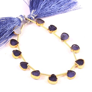 Könnte beinhalten: Eine Strähne aus dunkelvioletten Edelsteinperlen mit goldenen Akzenten. Die Perlen sind herzförmig und auf einer goldenen Kette aufgereiht. Die Strähne ist mit zwei blauen Quasten verziert.