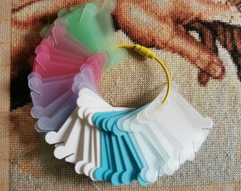 Könnte beinhalten: Ein Satz bunter Plastik-Fadenspulen für Stickerei oder Kreuzstich. Die Spulen sind in einem Kreis angeordnet und werden durch eine gelbe Schnur zusammengehalten. Die Spulen sind in Grün-, Rosa-, Weiß- und Blautönen.