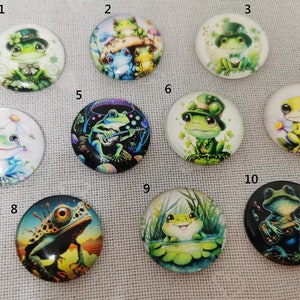 May include: Ten round glass cabochons with different frog designs. The frogs are depicted in various poses, including playing music, wearing hats, and sitting on lily pads. The cabochons are perfect for crafting projects, such as jewelry making, scrapbooking, and resin art.