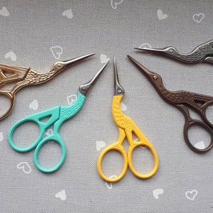 Op de afbeelding: Vijf paar decoratieve scharen met vogelvormige handvatten. De scharen zijn in verschillende kleuren, waaronder goud, teal, geel, bruin en zilver.