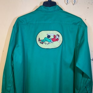 May include: A green long-sleeved shirt with a bowling-themed patch on the back. The patch features a cartoon illustration of a person bowling with a yellow background.