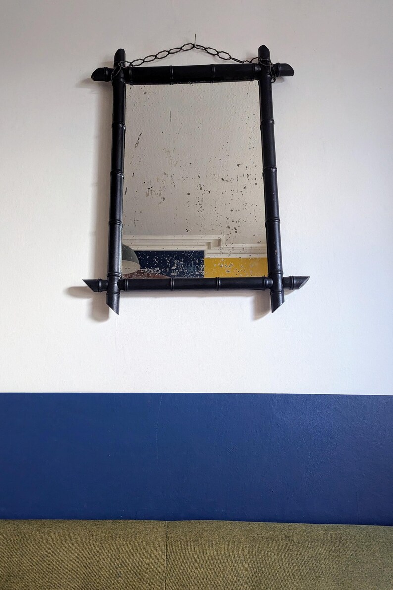 May include: A black framed mirror with a bamboo design hangs on a white wall with a blue accent wall below. The mirror has a chain hanging from the top.