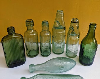 Puede incluir: Colección de siete botellas vintage de vidrio verde, algunas con letras en relieve, incluyendo "Champagne Cider Nottingham" y "Direct Aerated Ginger Beer".