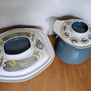 Op de afbeelding: Tweedelige serveerschaalset. De set bevat een ronde, afgedekte ovenschaal en een rechthoekige serveerschaal. Beide stukken zijn wit met een blauw interieur en hebben een decoratief patroon van groenten en paddenstoelen.