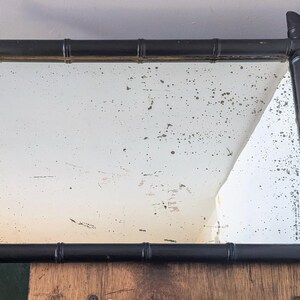 May include: A black framed mirror with a distressed, aged look. The frame is made of faux bamboo and has a rectangular shape.