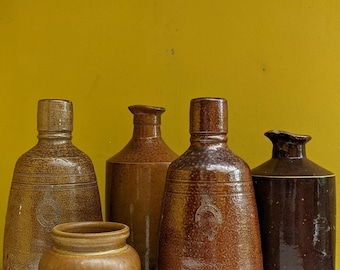 May include: Five brown stoneware pottery jars with a speckled glaze. The jars are various sizes and shapes. The largest jar has the text "CAMPOS, FILMES, AVENIDA, PORTUGAL" on the bottom.