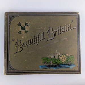 May include: A green and gold book cover with the title "Beautiful Britain" and a small illustration of a castle and a boat on the water.