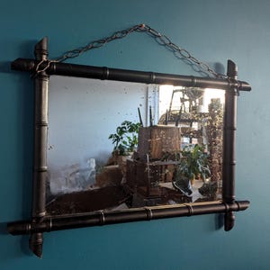 May include: A black framed mirror with a faux bamboo design. The mirror has a distressed look and is hanging on a blue wall.