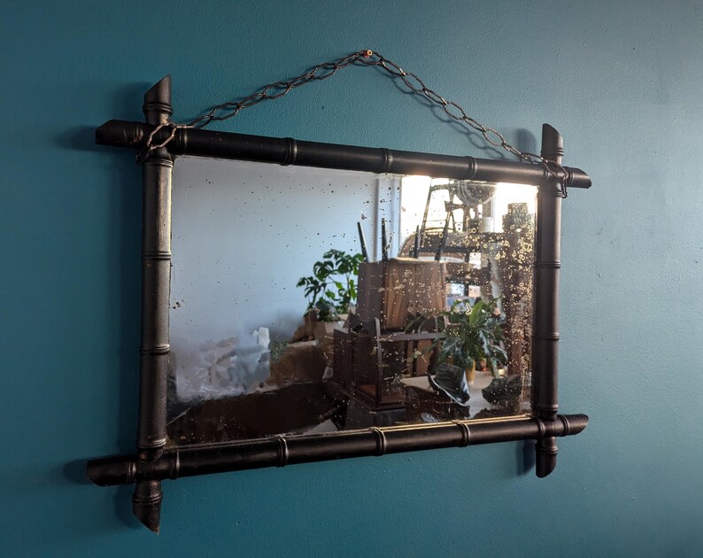 May include: A black framed mirror with a faux bamboo design. The mirror has a distressed look and is hanging on a blue wall.