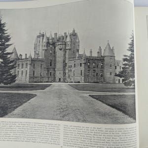 May include: A black and white photograph of a large, imposing castle with multiple towers and a long, winding driveway leading up to the front entrance. The castle is surrounded by a grassy lawn and trees.