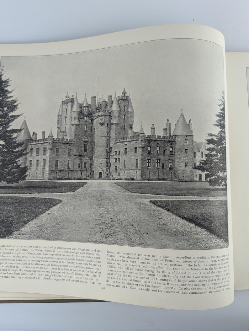 May include: A black and white photograph of a large, imposing castle with multiple towers and a long, winding driveway leading up to the front entrance. The castle is surrounded by a grassy lawn and trees.