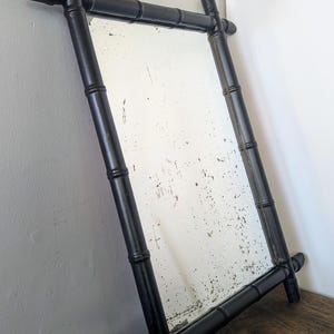 May include: A black bamboo framed mirror with a distressed glass surface. The frame is made of thick, black painted bamboo.