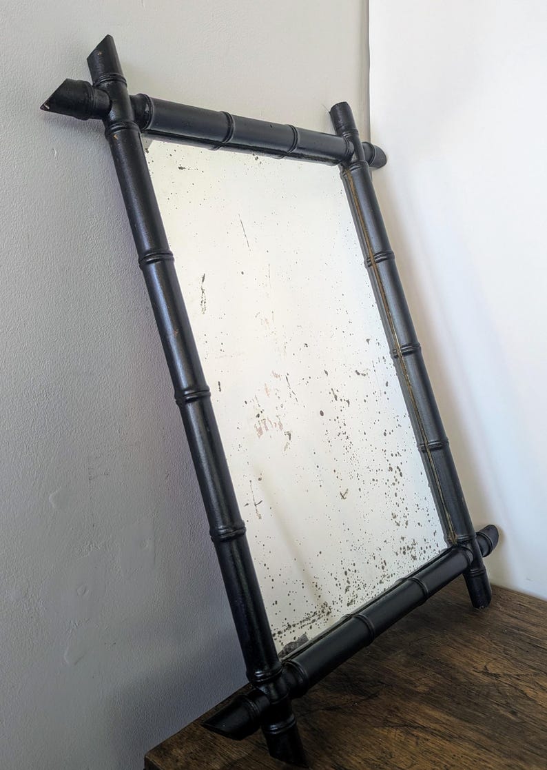 May include: A black bamboo framed mirror with a distressed glass surface. The frame is made of thick, black painted bamboo.