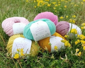 May include: Six balls of yarn in various colors, including pink, green, yellow, and purple. The yarn is labeled "Laine du Nord" and "Dolly 125".