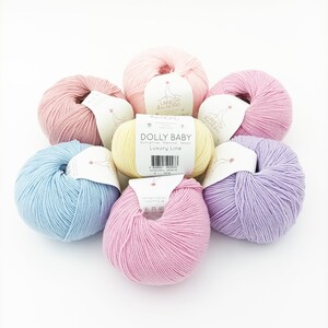 May include: Six balls of yarn in various pastel colours, including light pink, pale yellow, baby blue, lavender, and a deeper pink. The yarn is labelled "Dolly Baby" and "Luxury Line" with a barcode.