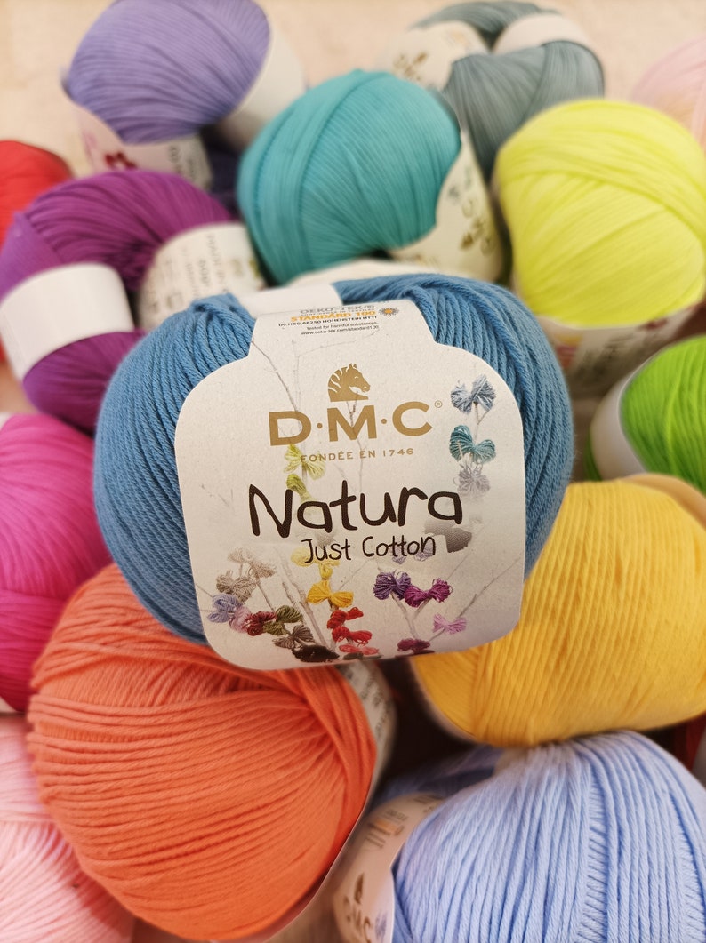 May include: A close-up of a variety of colourful yarn balls, including blue, green, yellow, orange, pink, and purple. The yarn is labelled "DMC Natura Just Cotton".