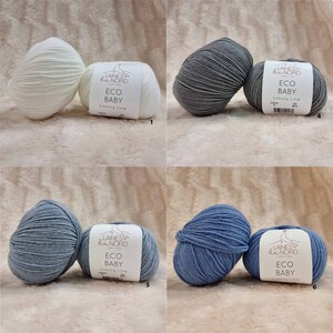 May include: Four balls of yarn in different colors: white, gray, light blue, and dark blue. Each ball has a label that reads "Laines du Nord ECO BABY Luxury Line".