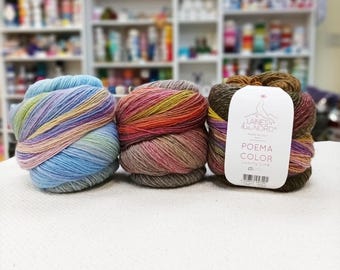 May include: Three colorful yarn skeins. The skeins are in shades of blue, pink, orange, and brown. One skein has a tag that reads "POEMA COLOR". The yarn is likely for knitting or crochet projects.