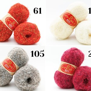 Puede incluir: Cuatro ovillos de lana en diferentes colores: naranja, blanco, gris y rojo. Cada ovillo tiene una etiqueta roja con el texto "Stenli Rossi". Los ovillos est&aacute;n etiquetados con los n&uacute;meros: 61, 102, 105 y 219.