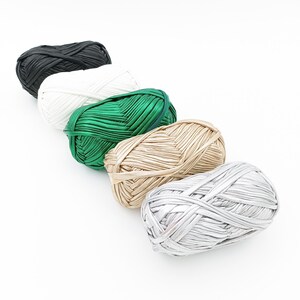 May include: Five balls of yarn in different colors: black, white, green, gold, and silver. The yarn is made of a soft, silky material and is perfect for knitting or crocheting.